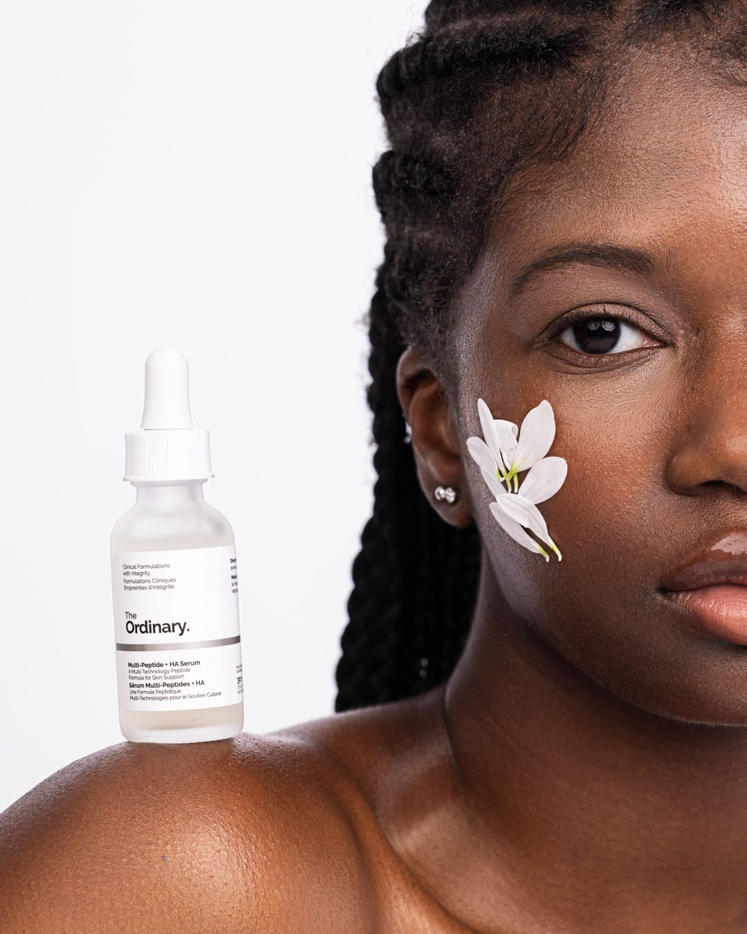 Skincare-Porträt eines Models mit Serumflasche und weißer Blüte