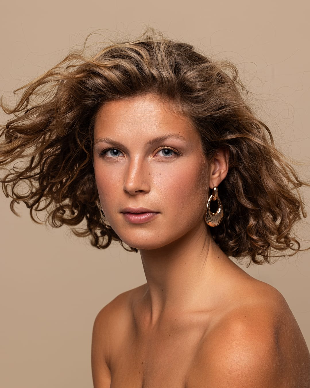Beauty-Porträt eines Models mit lockigem Haar und goldfarbenen Ohrringen